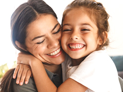 Image of happy family mother and little daughter hugging while having breakfast at home in morning